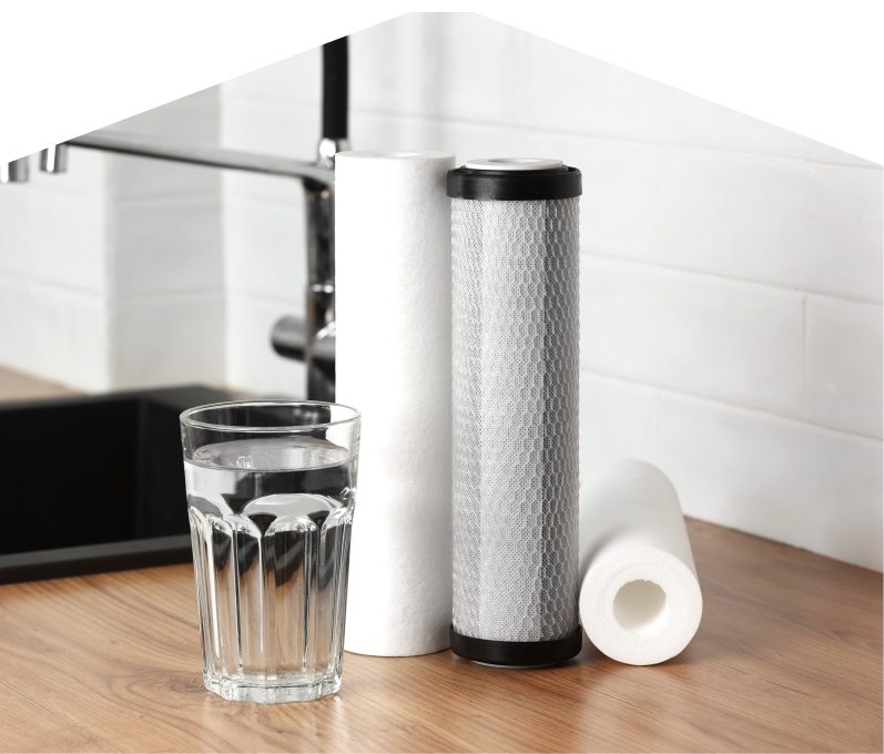 Set of Home Aire Care water filtration cartridges placed beside a clear glass of water on a kitchen countertop, with a sink and modern faucet in the background. Set of Home Aire Care water filtration cartridges placed beside a clear glass of water on a kitchen countertop, with a sink and modern faucet in the background.