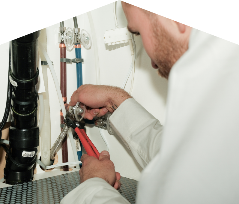 Home Aire Care plumbing expert tightening connections under a sink during a faucet installation, surrounded by hot and cold water supply lines and PVC drainage. Home Aire Care plumbing expert tightening connections under a sink during a faucet installation, surrounded by hot and cold water supply lines and PVC drainage.