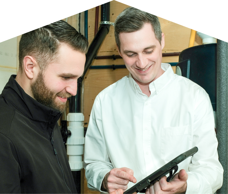 Home Aire Care specialist reviewing maintenance plan options with a smiling homeowner using a tablet, inside a utility room with visible piping. Home Aire Care specialist reviewing maintenance plan options with a smiling homeowner using a tablet, inside a utility room with visible piping.