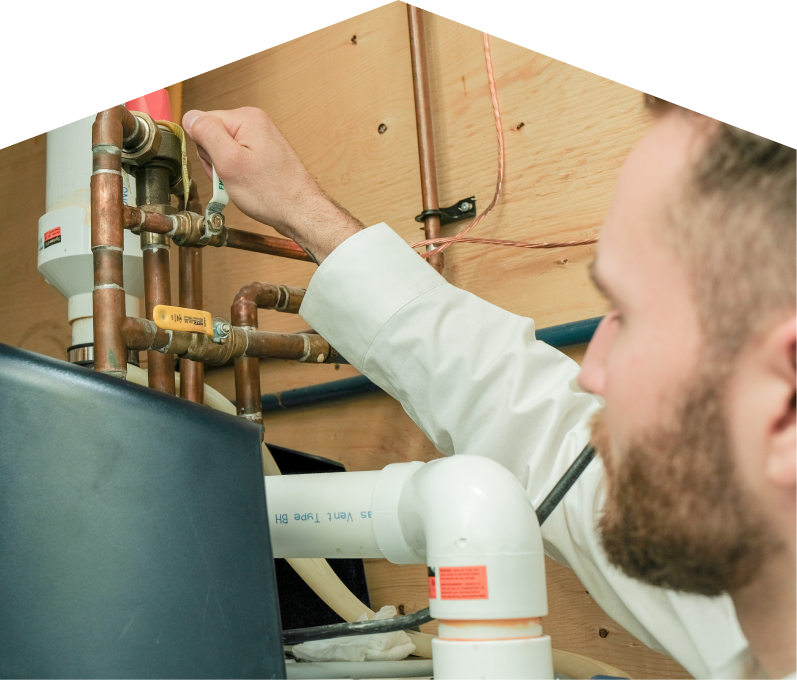 Home Aire Care water heater specialist tightens a valve on copper piping during a water heater installation, with exposed wood paneling and wiring in the background. Home Aire Care water heater specialist tightens a valve on copper piping during a water heater installation, with exposed wood paneling and wiring in the background.